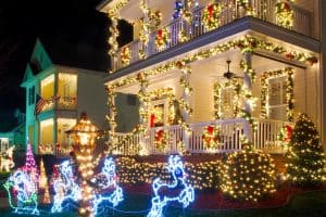 Home in neighborhood decorated with garlands and bright white and colorful LED Christmas lights, including a porch and light-up reindeer figures on the lawn.